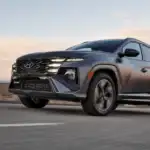 2026 Hyundai Tucson gray SUV driving on desert road at sunset with LED headlights and bold grille.