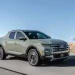 2026 Hyundai Santa Cruz gray pickup driving on highway with desert landscape and blue sky.