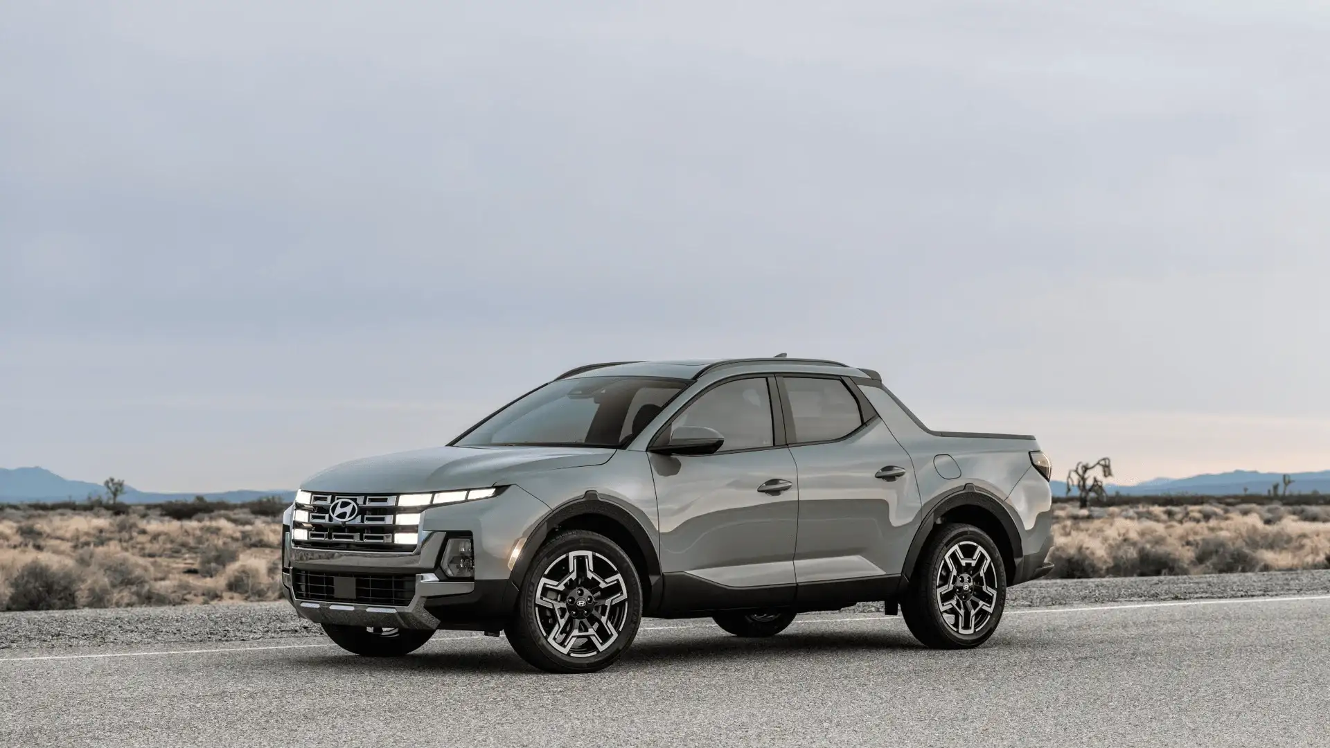 2026 Hyundai Santa Cruz gray pickup shown on desert road with LED lights and alloy wheels.