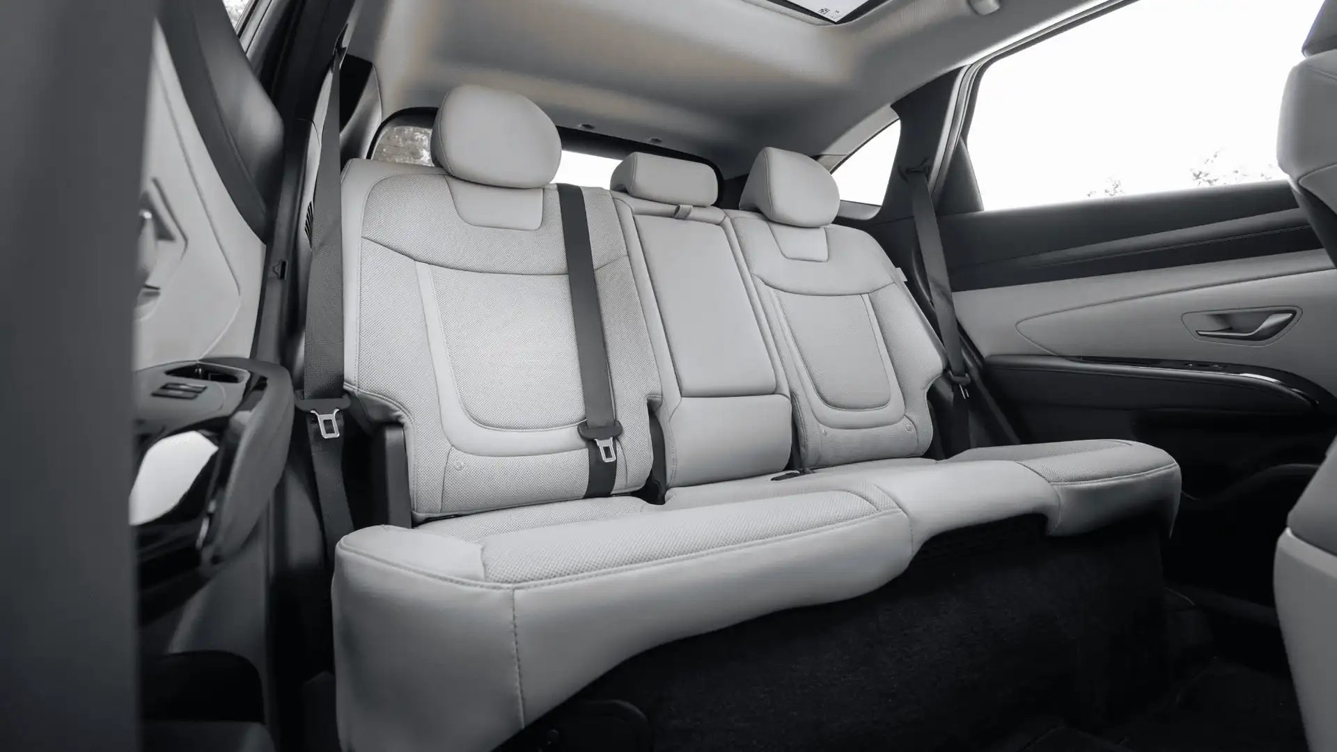 2026 Hyundai Tucson Hybrid rear cabin with light seats, seatbelts, and panoramic roof.