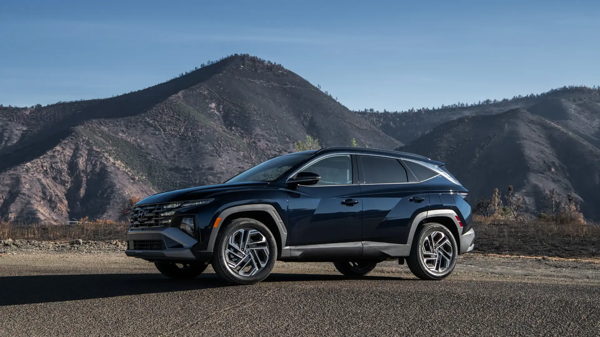 2026 Hyundai Tucson Hybrid black SUV parked roadside with mountain hills in the background.