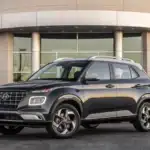 2026 Hyundai Venue gray compact SUV parked outside modern building with roof rails and alloy wheels.