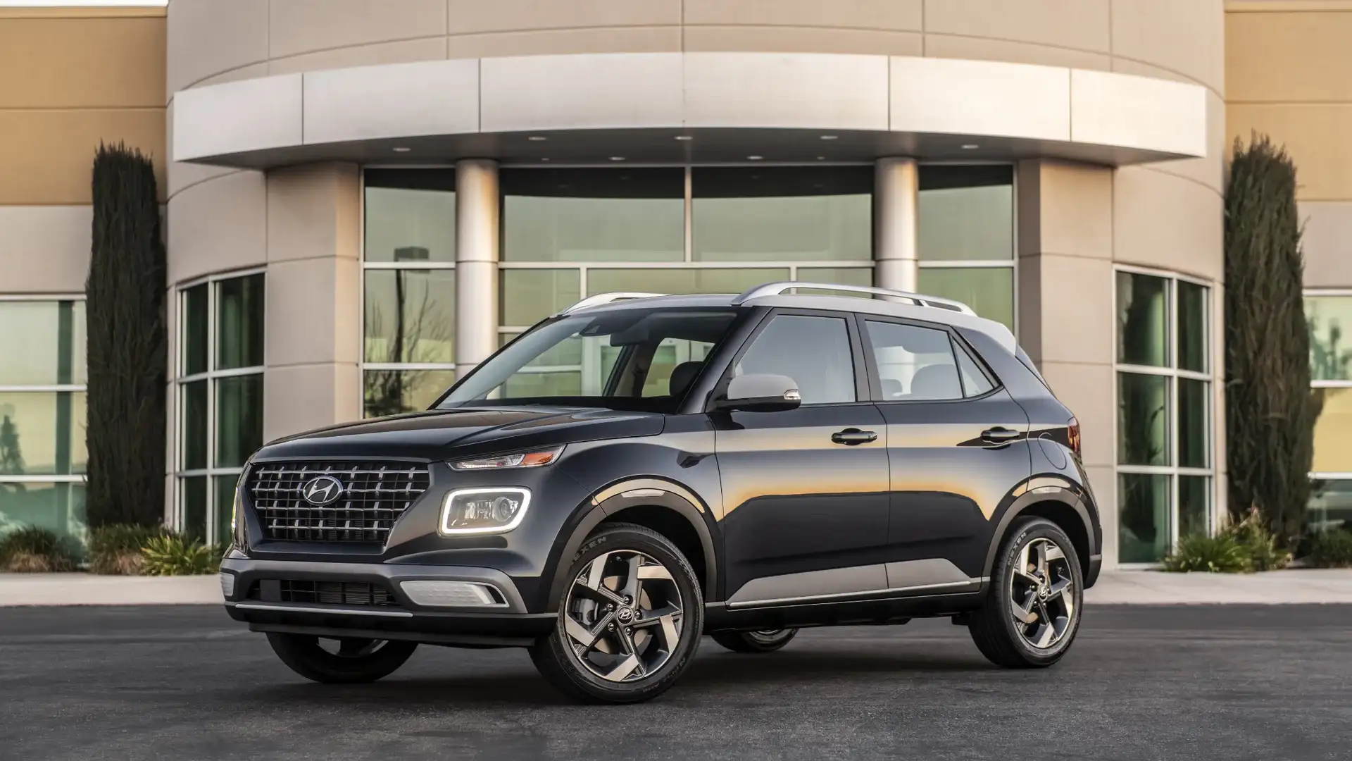 2026 Hyundai Venue gray compact SUV parked outside modern building with roof rails and alloy wheels.