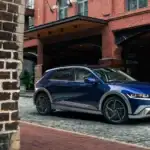 2027 Hyundai IONIQ 5 blue electric SUV parked on cobblestone street near brick building.