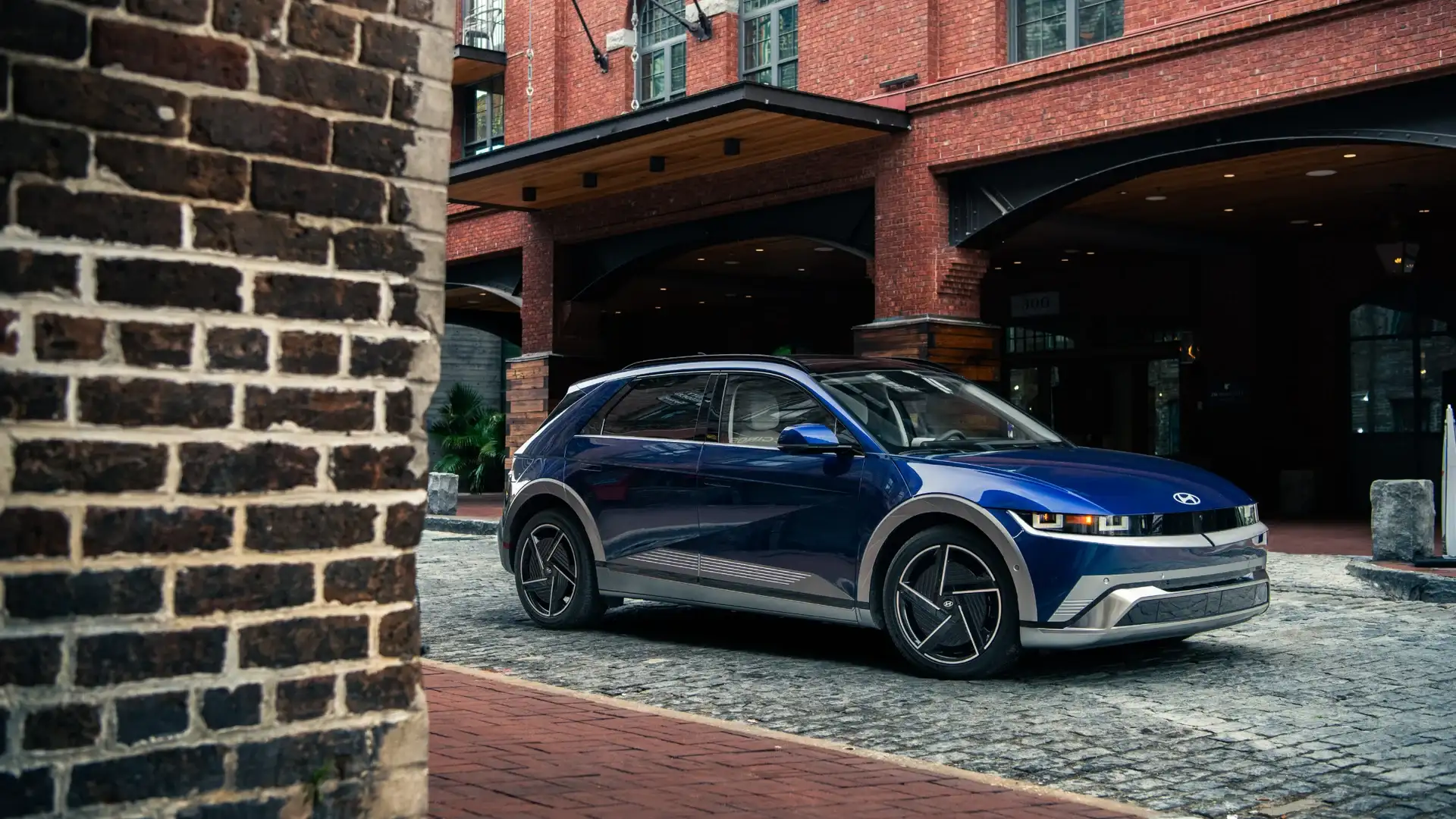 2027 Hyundai IONIQ 5 blue electric SUV parked on cobblestone street near brick building.