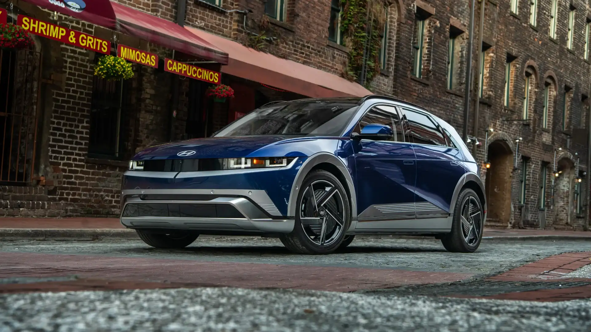 2027 Hyundai IONIQ 5 blue electric SUV parked on city street near brick storefronts.