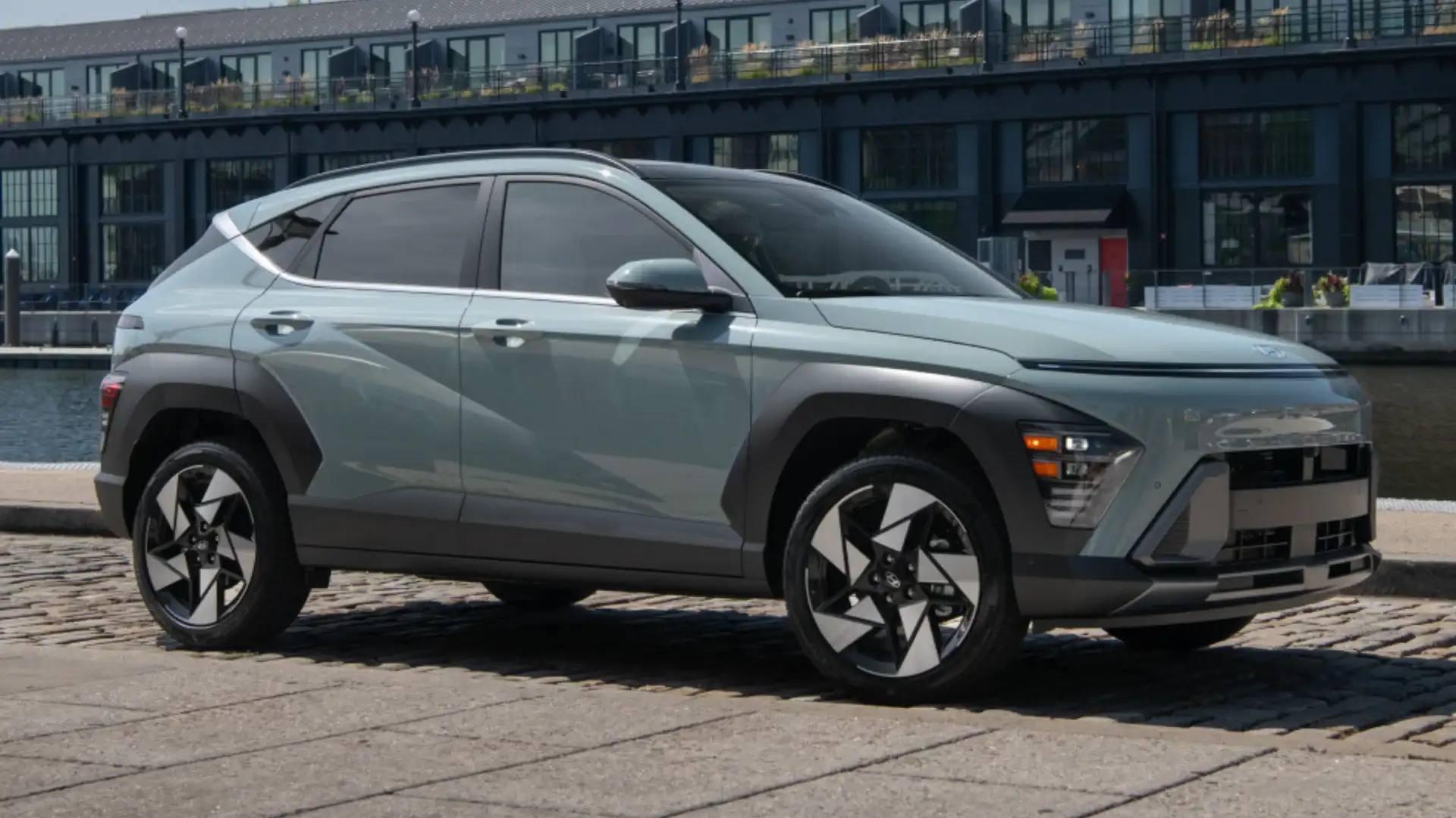 2027 Hyundai Kona gray compact SUV parked on cobblestone street beside brick building.