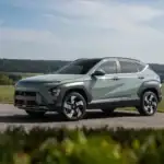2027 Hyundai Kona gray compact SUV shown in side profile on rural road with green hills.