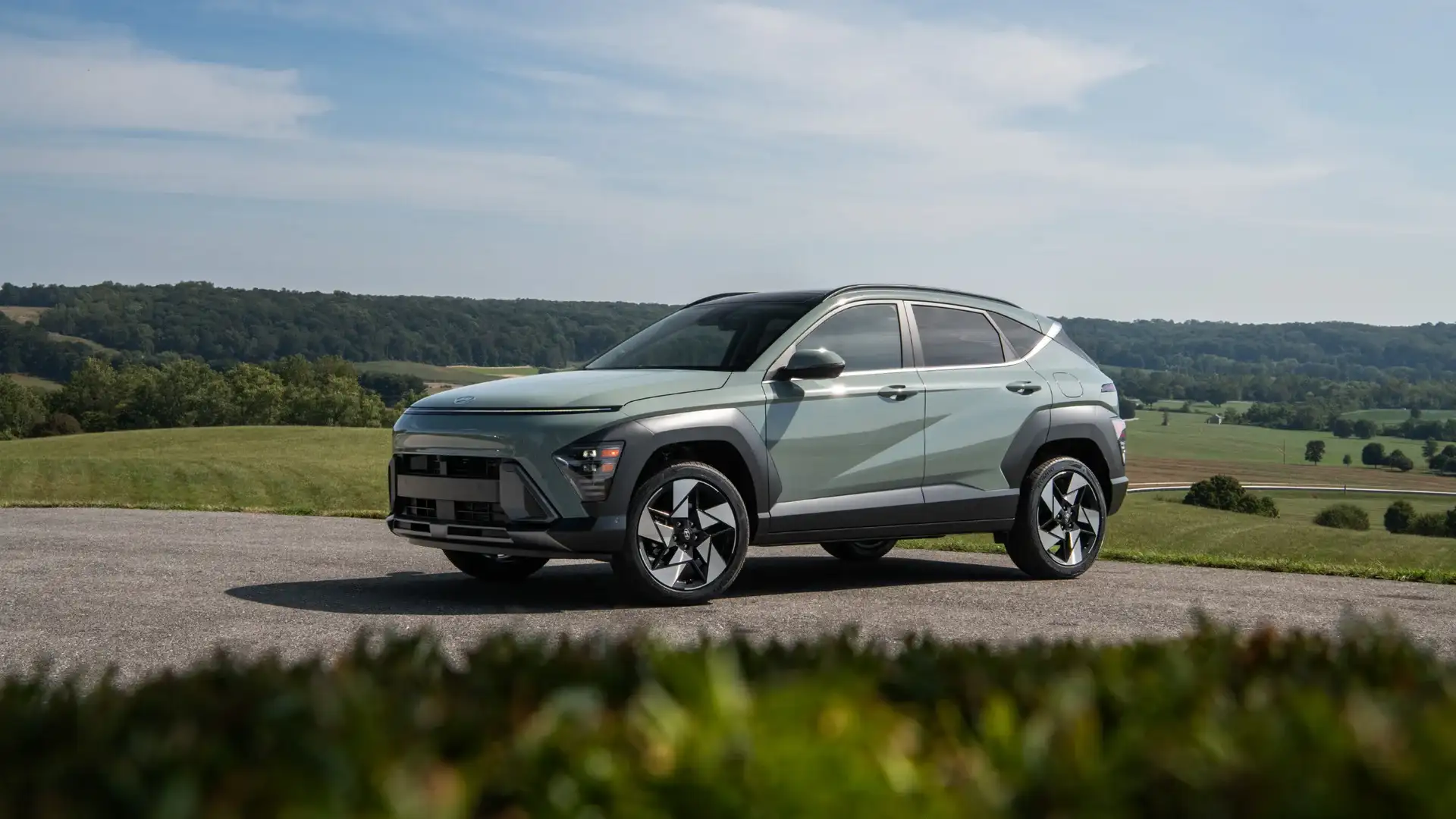 2027 Hyundai Kona gray compact SUV shown in side profile on rural road with green hills.
