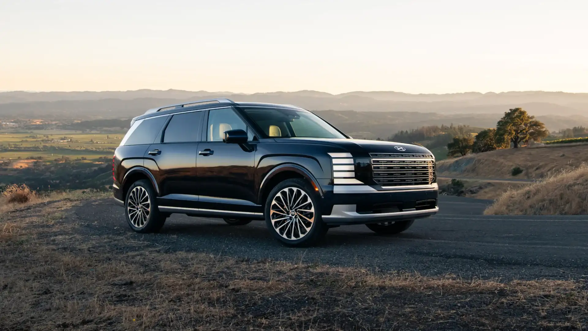 2027 Hyundai Palisade black SUV parked on mountain road at sunset with chrome grille.