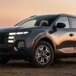 2027 Hyundai Santa Cruz gray pickup truck shown from front angle on rugged hillside at sunset.