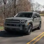 2027 Hyundai Santa Fe gray SUV driving on winding forest road with front LED lighting.