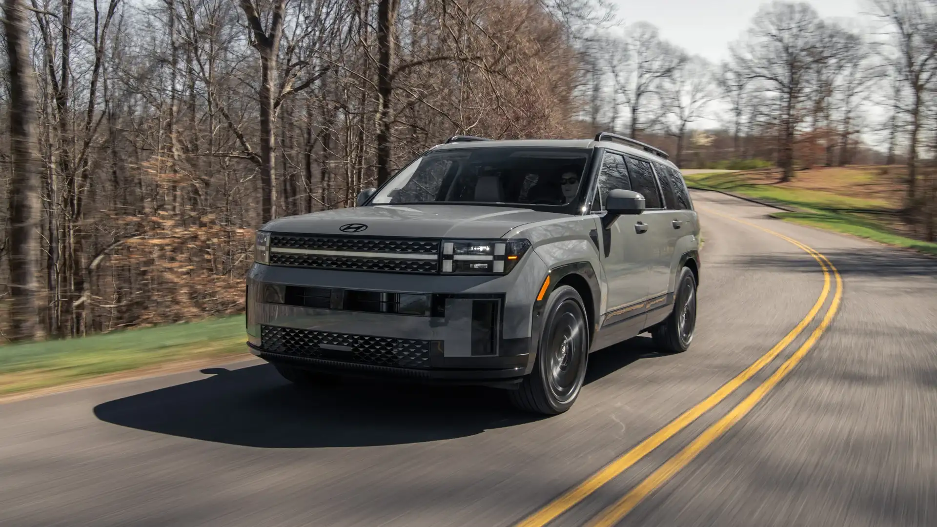 2027 Hyundai Santa Fe gray SUV driving on winding forest road with front LED lighting.
