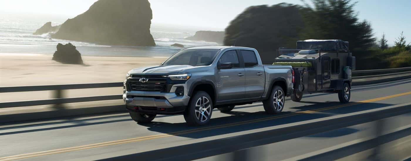 A silver 2023 Chevy Colorado Z71 towing a camper on a coastal road.