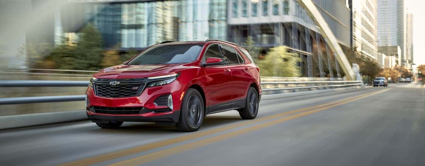 A red 2024 Chevy Equinox RS driving across a bridge after visiting a Chevy dealer near Seabrook.