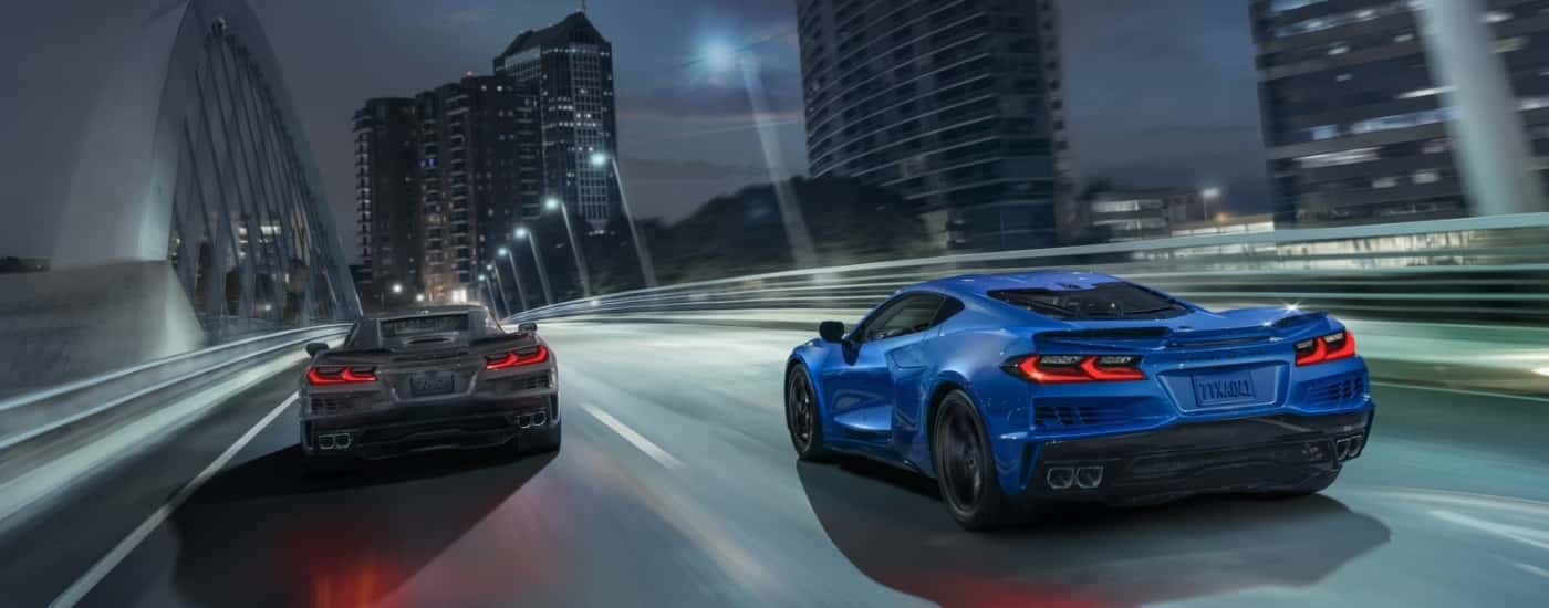 A grey and a blue 2025 Chevy Corvette E-Ray are shown driving over a bridge at night.