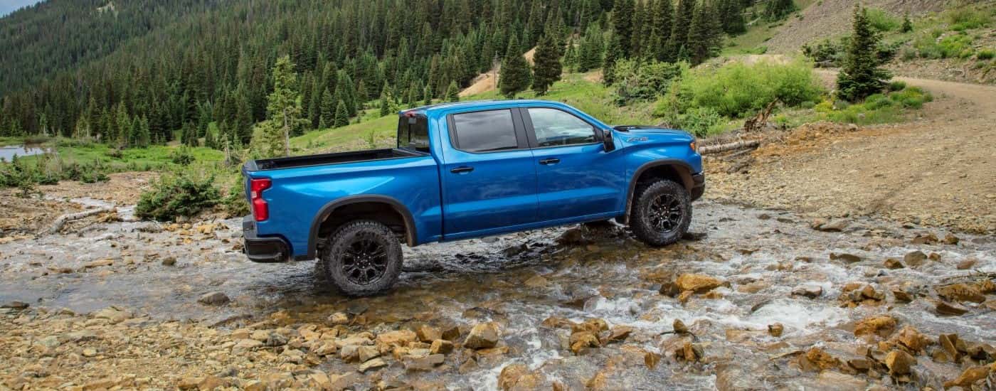 A blue 2024 Chevy Silverado 1500 ZR2 is driving through a creek.