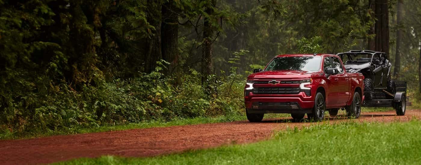 A red 2025 Chevy Silverado 1500 for sale is towing an ATV.