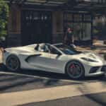 A white 2025 Chevy Corvette for sale in front of a clothing shop.