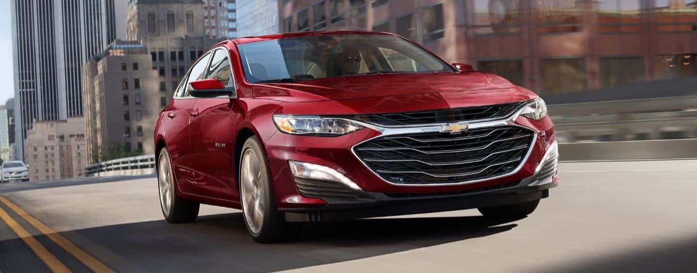 A red 2024 Chevy Malibu driving in a city from a Chevy dealer near Danville.