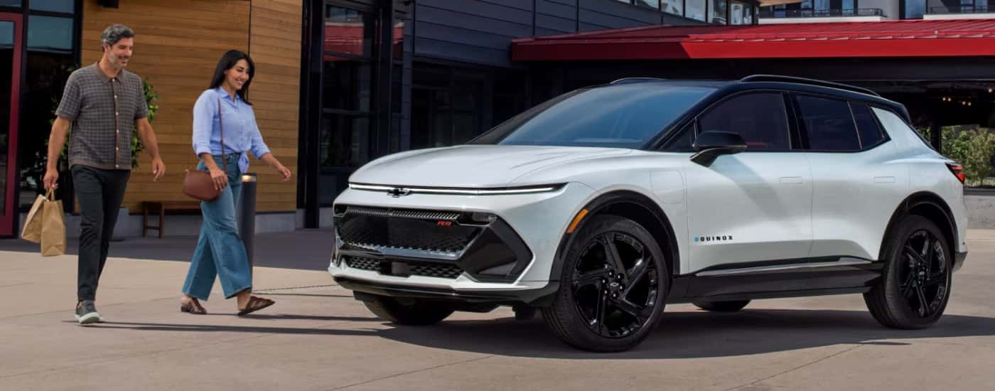 People are shown walking toward a white 2025 Chevy Equinox EV RS.