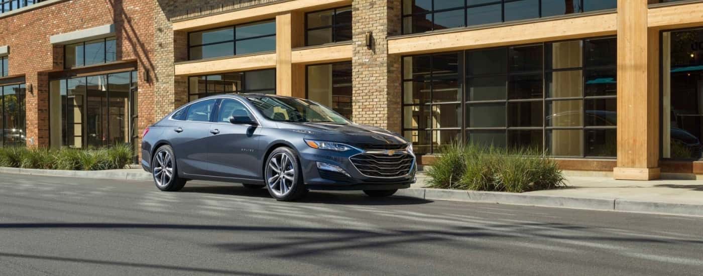 A grey 2024 Chevy Malibu is shown from the front at an angle after leaving a Chevy dealer near Portsmouth.