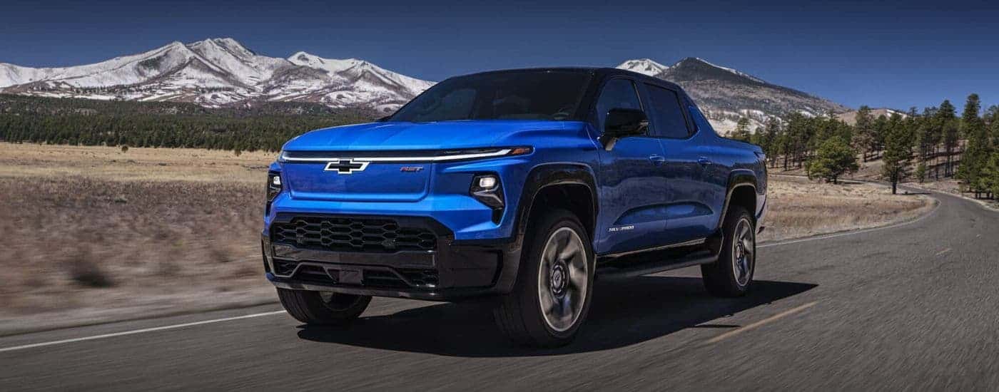 A blue 2024 Chevy Silverado EV RST is shown driving to a Chevy dealer in Amesbury.