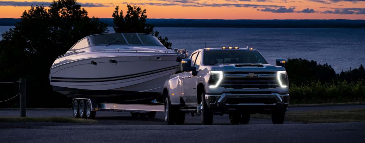 A white 2024 Chevy Silverado 3500 HD LTZ is shown from the front a while towing a boat.
