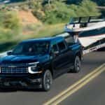 A black 2027 Chevy Silverado 1500 High Country towing a boat on a highway.
