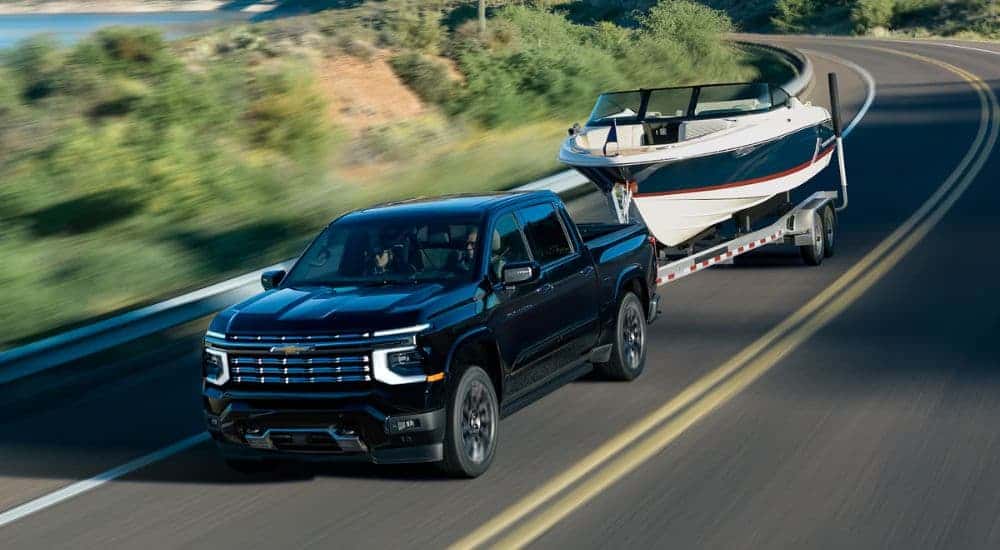 A black 2027 Chevy Silverado 1500 High Country towing a boat on a highway.