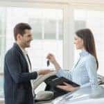 saleswoman is handing car keys to man inside showroom