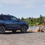 blue 2024 nissan rogue parked on gravel by a body of water with a family and dog