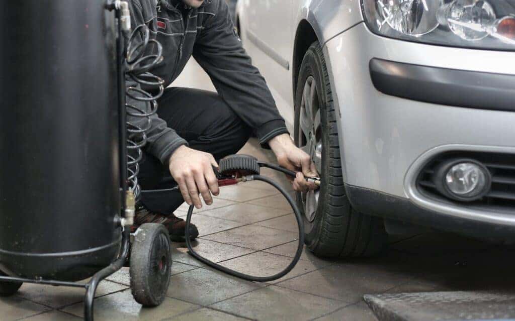 Man in Black Jacket and Black Pants Sitting Near Silver Vehicle filling up tire