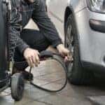 Man in Black Jacket and Black Pants Sitting Near Silver Vehicle filling up tire