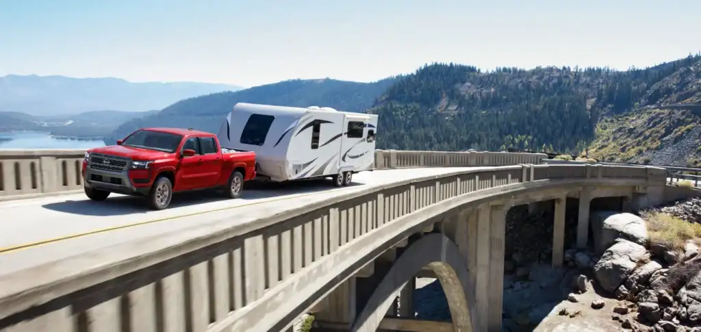 red 2026 nissan frontier truck towing a trailer across a bridge highway