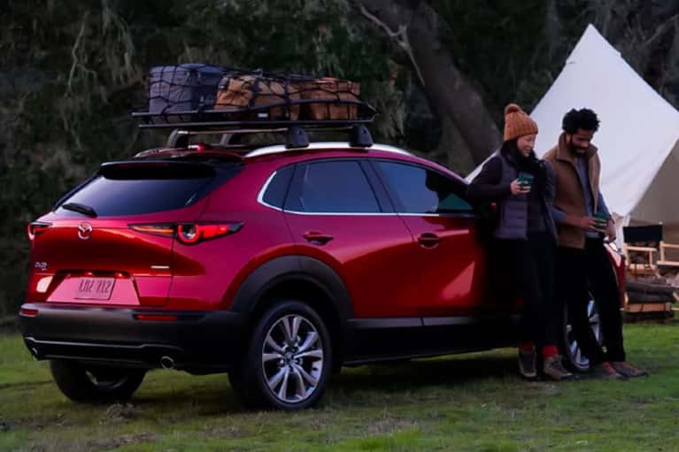 Couple are camping and are outside leaning against a brand new red Mazda SUV.