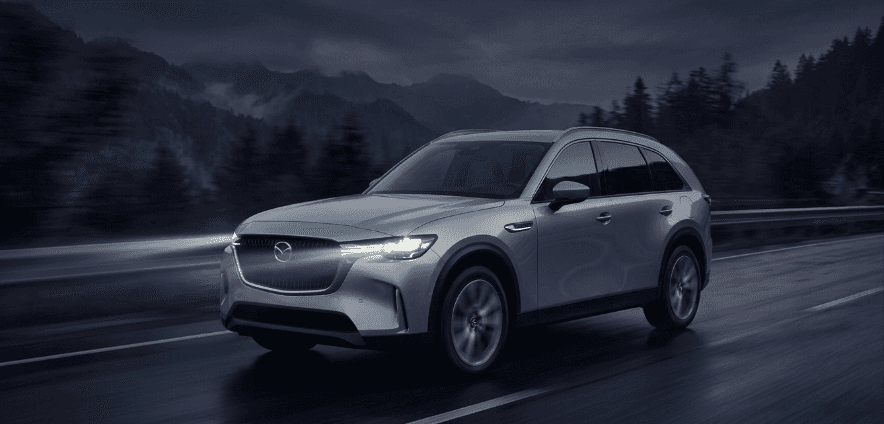 2026 Mazda CX-90 luxury crossover SUV driving on a moody mountain highway at twilight — available at Beaver Mazda in Cumming, GA