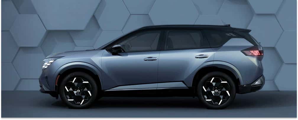 Side profile view of a silver two-tone 2027 Nissan Rogue Hybrid SUV against a textured wall background.