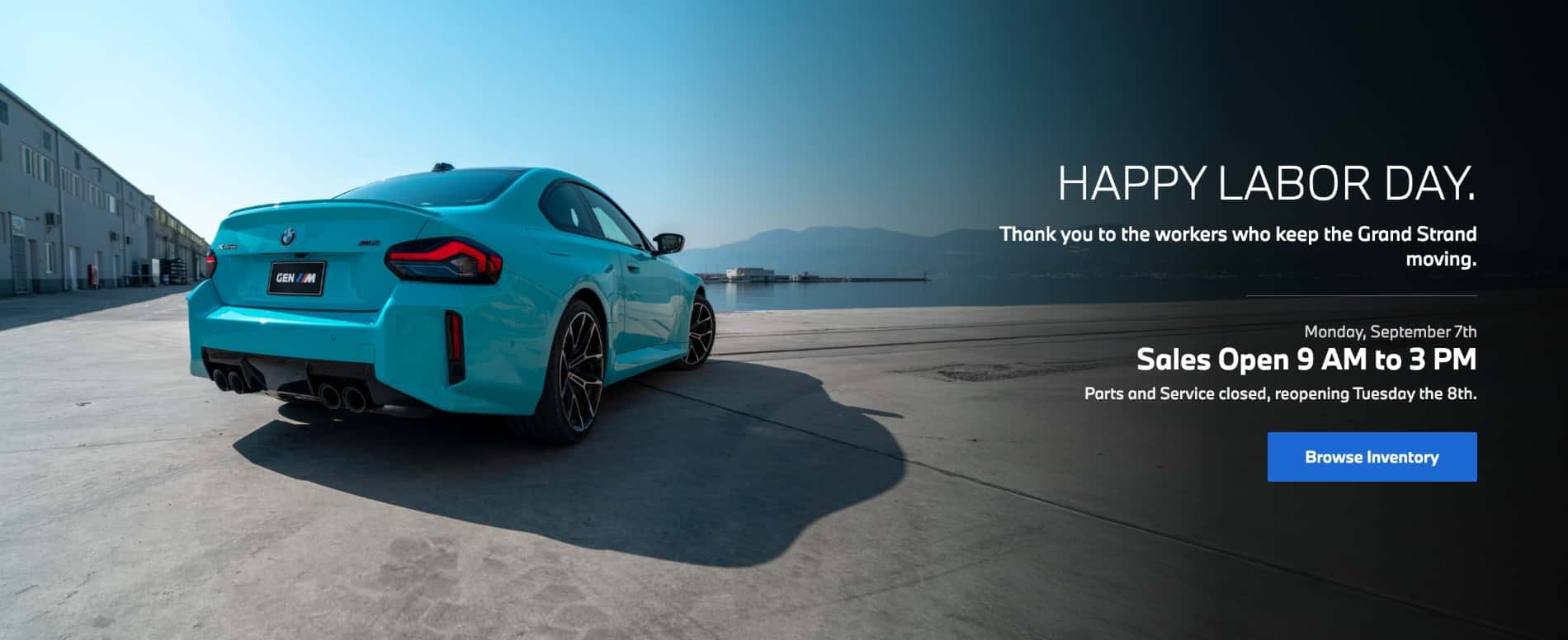 BMW M2 coupe parked beside the waterfront with Labor Day holiday hours for BMW of Myrtle Beach showing Sales open 9 AM to 3 PM and Parts and Service closed.