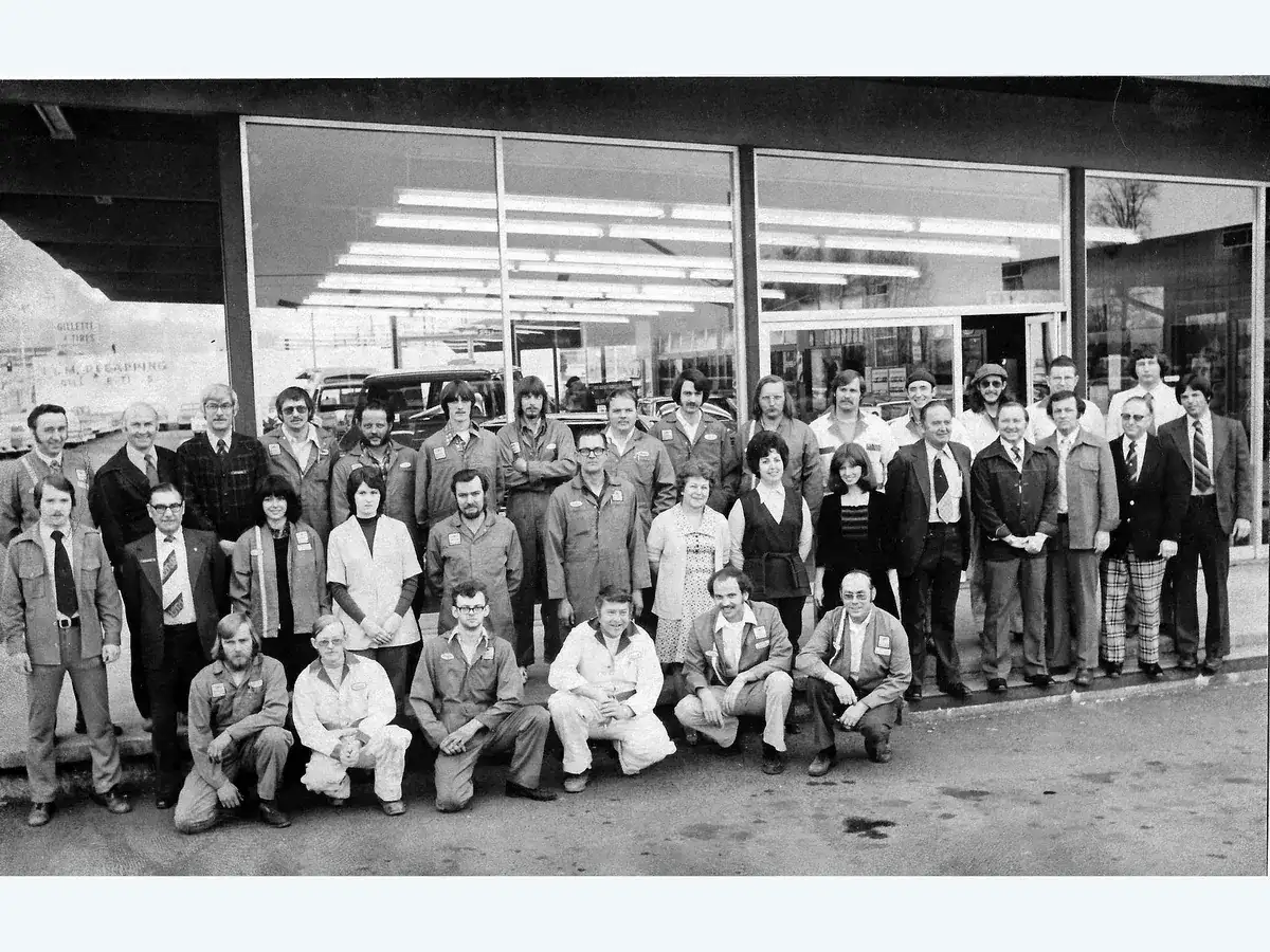 About forty members of the Bud Clary Chevrolet team in work jackets and suits, posed in rows in front of the showroom windows in 1976