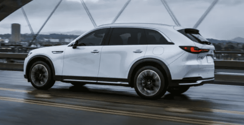 2026 Mazda CX-90 PHEV driving across a wet city bridge