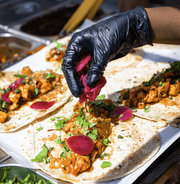 Street food chef garnishing freshly prepared tacos with pickled onions