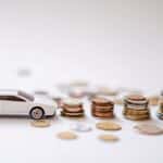 White toy sports car beside stacks of coins on a white background, emphasizing savings and finance.
