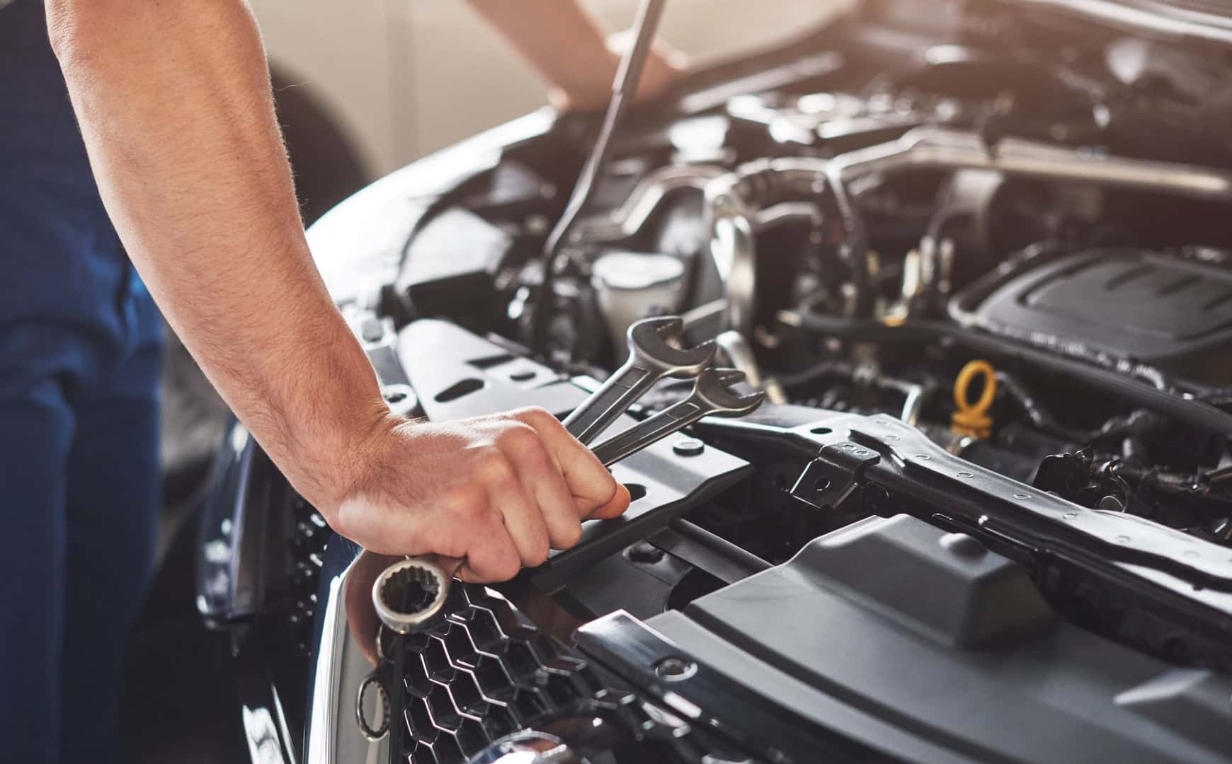 person with wrenches and other tools looking under the hood of a vehicle