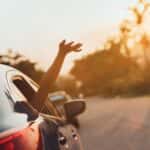 car driving on a sunny day with the passenger hanging their hand out the window
