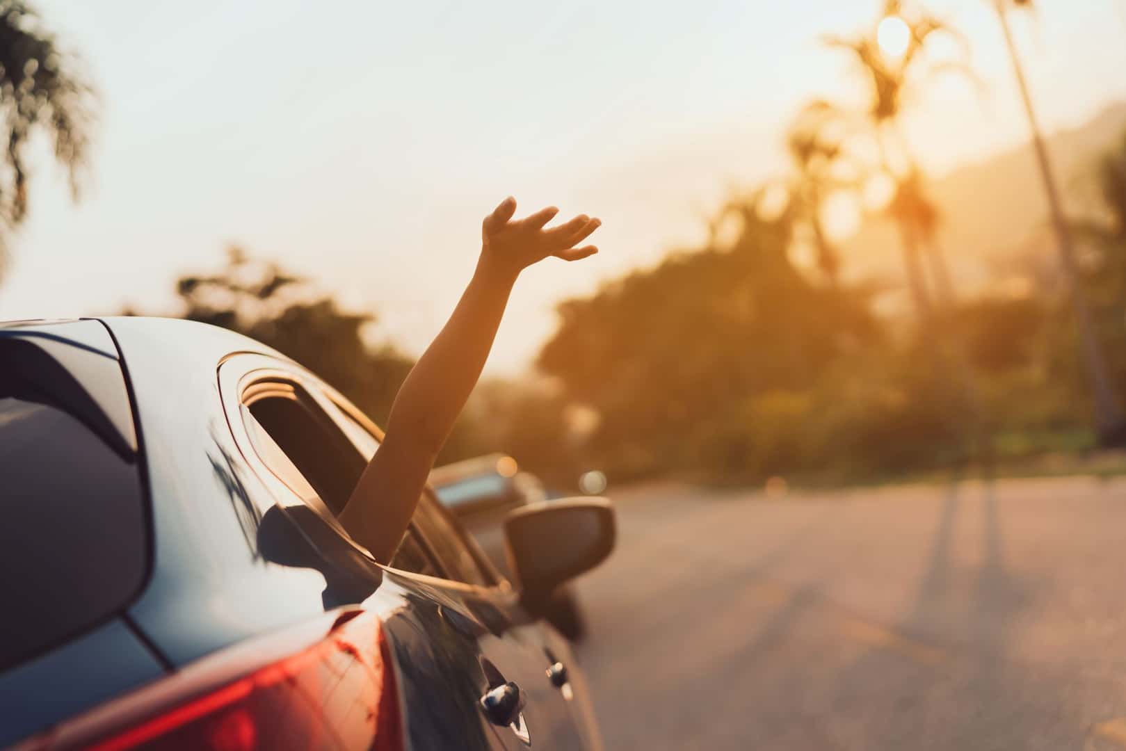 car driving on a sunny day with the passenger hanging their hand out the window