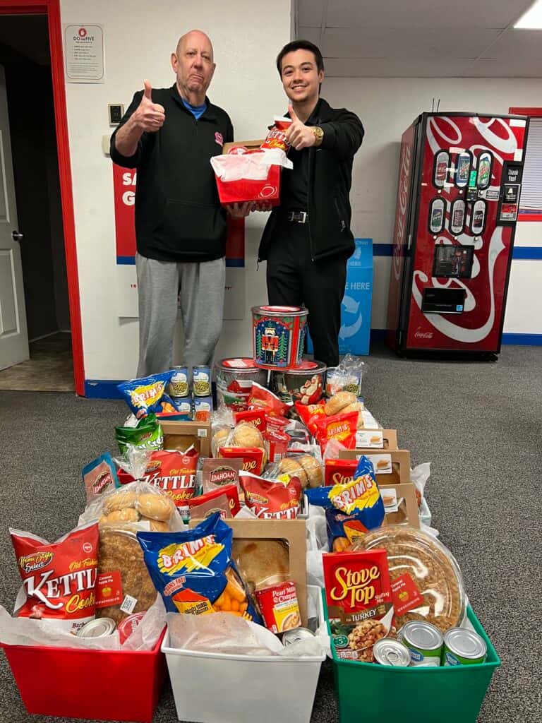 The CarHop of Des Moines team posing in front of a display of Thanksgiving baskets filled with pumpkin pies, ready to be given to customers as part of the CarHop Cares initiative.