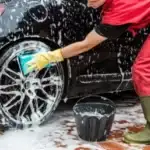 person washing their car with a scrub soap and bucket