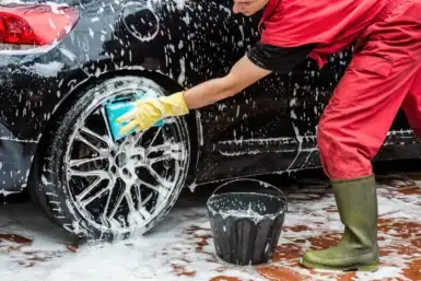 person washing their car with a scrub soap and bucket