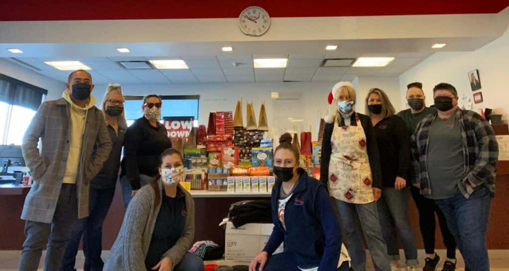 The CarHop of Fort Collins team posing inside the FoCo Cafe with their donations, including office supplies, a new KitchenAid mixer, grab-and-go food, and wrapped gifts for children.